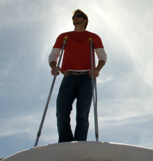 Man on mountain with crutches against blue sky.